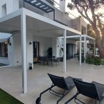 Terraza de vivienda con pérgolas de aluminio blancas, comedor exterior, zona de descanso y piscina