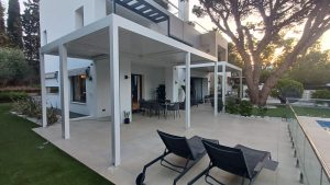 Terraza de vivienda con pérgolas de aluminio blancas, comedor exterior, zona de descanso y piscina