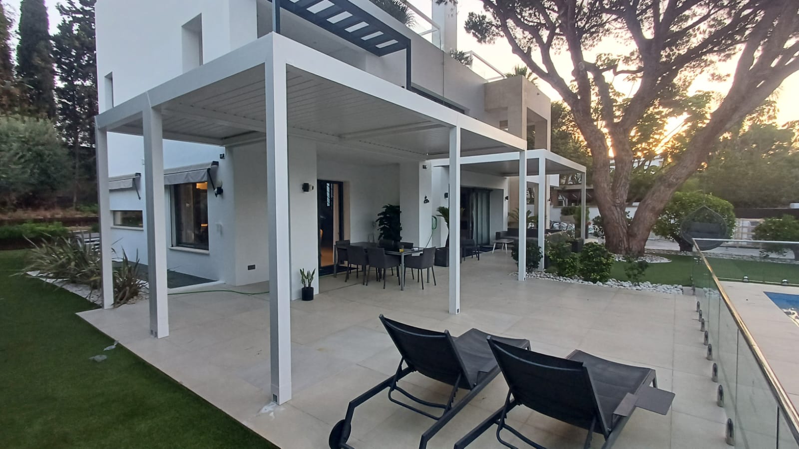 Terraza de vivienda con pérgolas de aluminio blancas, comedor exterior, zona de descanso y piscina
